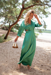 Robe fluide à manches trois-quarts portée par une femme, vue de trois-quarts, sandales à la main, plage