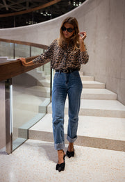 Gilet léopard boutonné porté par une femme, vue de trois-quarts, escalier, lunettes de soleil, jean