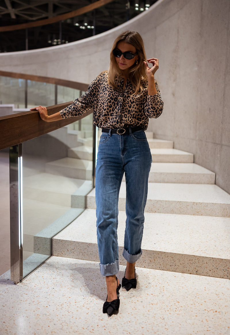 Gilet léopard boutonné porté par une femme, vue de trois-quarts, escalier, lunettes de soleil, jean