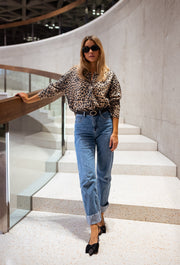 Gilet léopard boutonné porté par une femme, silhouette entière, escalier, rampe en verre, lunettes de soleil
