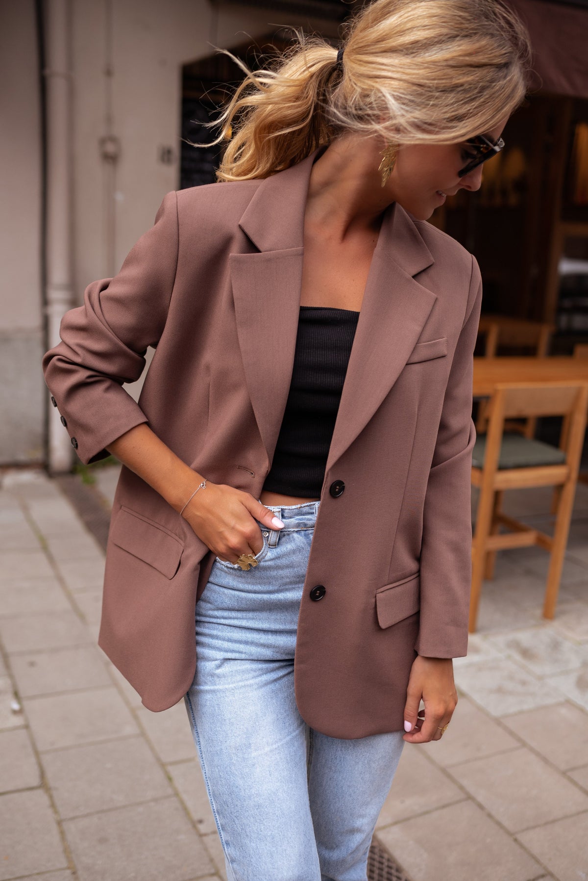 Blazer ample à épaulettes porté par une femme, vue rapprochée, main sur le col, jean clair