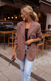 Blazer ample à épaulettes porté par une femme, vue de trois-quarts, lunettes de soleil à la main