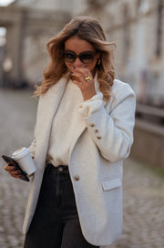 Blazer effet laine à épaulettes porté par une femme, vue rapprochée, lunettes de soleil, téléphone, main au col