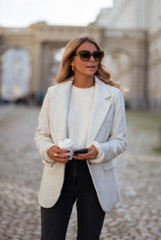 Blazer effet laine à épaulettes porté par une femme, vue de trois-quarts, lunettes de soleil, téléphone, pavés