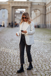 Blazer effet laine à épaulettes porté par une femme, silhouette entière, bottines noires, téléphone, pavés
