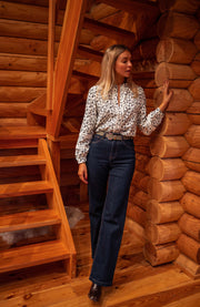 Blouse fluide à motifs portée par une femme, silhouette entière, escalier en bois, jean