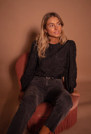 Blouse à poignets élastiques portée par une femme, assise, sur un fauteuil rose, jean noir
