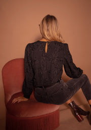 Blouse à poignets élastiques portée par une femme, vue de dos, fauteuil rose, manches bouffantes
