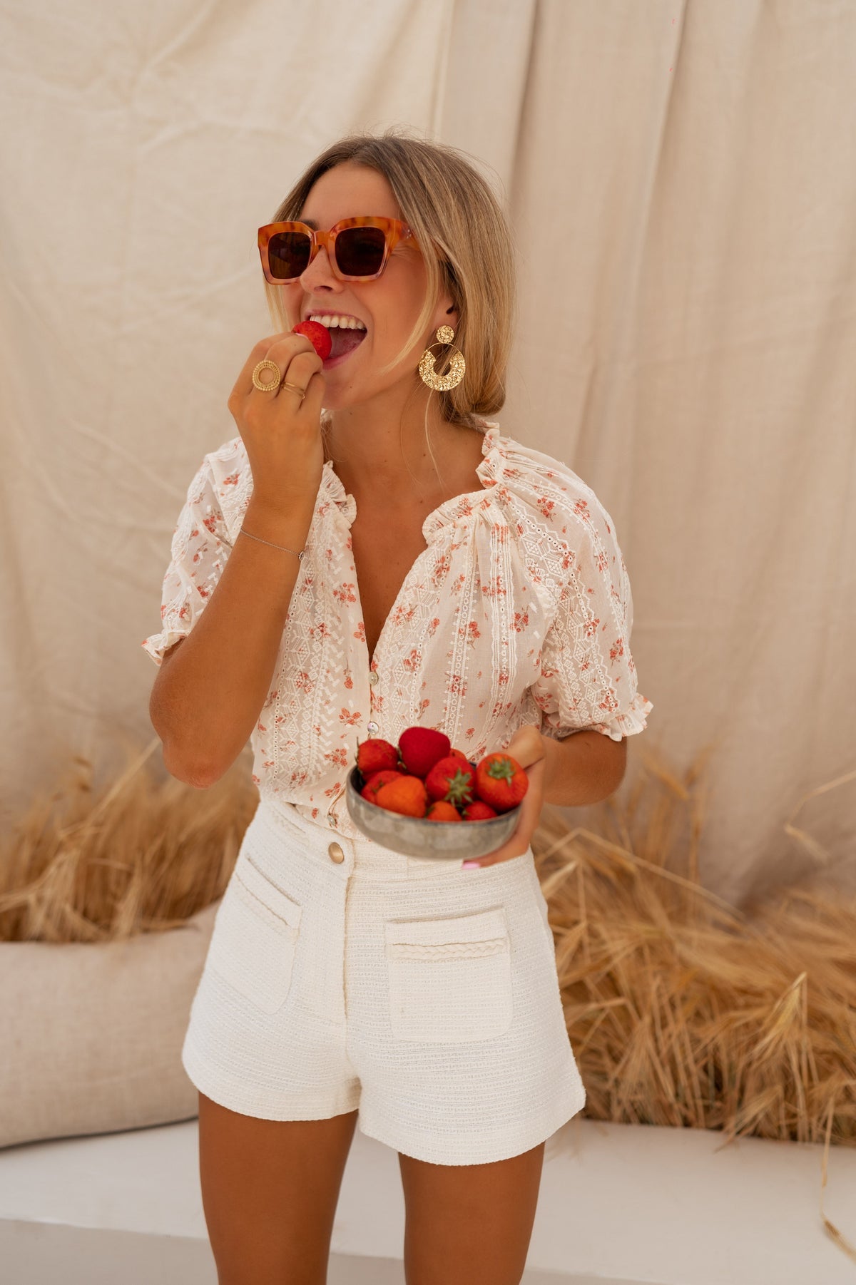 Blouse brodée à col V portée par une femme, silhouette entière, fraises, short blanc