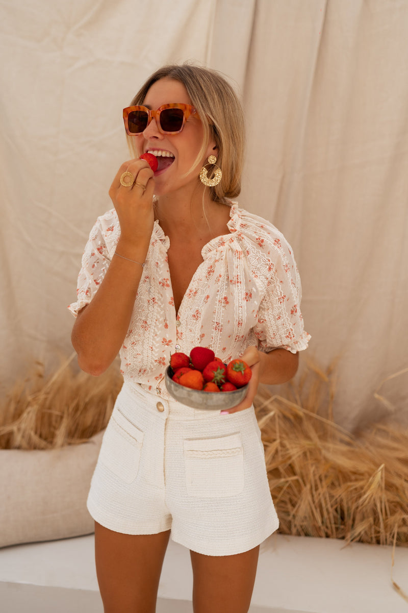 Blouse brodée à col V portée par une femme, silhouette entière, fraises, short blanc