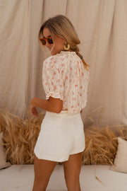 Blouse brodée à col V portée par une femme, vue de trois-quarts, lunettes, main dans les cheveux
