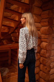 Blouse fluide à motifs portée par une femme, vue de trois-quarts, cheveux longs, bois, regard sur le côté