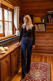 Blouse courte en dentelle portée par une femme, silhouette entière, tapis, jean, pièce en bois