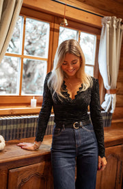 Blouse courte en dentelle portée par une femme, vue de trois-quarts, appuyée à un meuble, jean