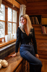 Blouse courte en dentelle portée par une femme, assise, sur un meuble en bois, jean foncé