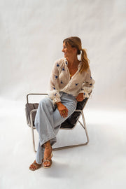 Blouse transparente à fleurs brodées portée par une femme, assise, chaise en métal, jean large