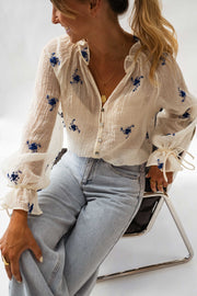 Blouse transparente à fleurs brodées portée par une femme, assise, fauteuil noir, jean large
