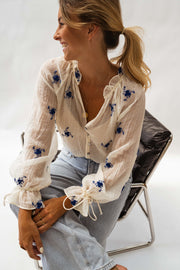 Blouse transparente à fleurs brodées portée par une femme, assise, fauteuil noir, sourire
