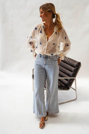 Blouse transparente à fleurs brodées portée par une femme, vue de face, fauteuil noir, sandales
