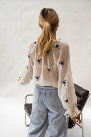 Blouse transparente à fleurs brodées portée par une femme, vue de dos, fauteuil noir, queue-de-cheval