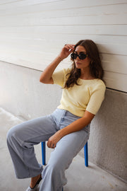 Blouse dos ouvert à nouer jaune portée par une femme, assise, lunettes de soleil, tabouret bleu