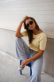 Blouse dos ouvert à nouer jaune portée par une femme, assise, lunettes de soleil, mur gris