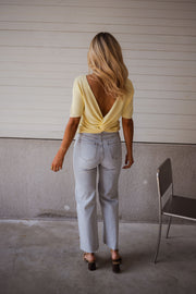 Blouse dos ouvert à nouer jaune portée par une femme, vue de dos, mur gris, dos ouvert