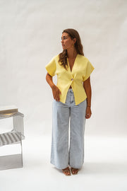 Blouse évasée à col V jaune portée par une femme, vue de face, chaise métallique, jean large