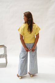 Blouse évasée à col V jaune portée par une femme, vue de dos, jean large, chaise grise
