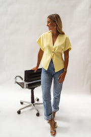 Blouse évasée à col V jaune portée par une femme, vue de face, chaise noire, jean clair