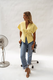 Blouse évasée à col V jaune portée par une femme, vue de face, ventilateur, chaise noire