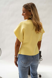 Blouse évasée à col V jaune portée par une femme, vue de dos, chaise noire, jean clair