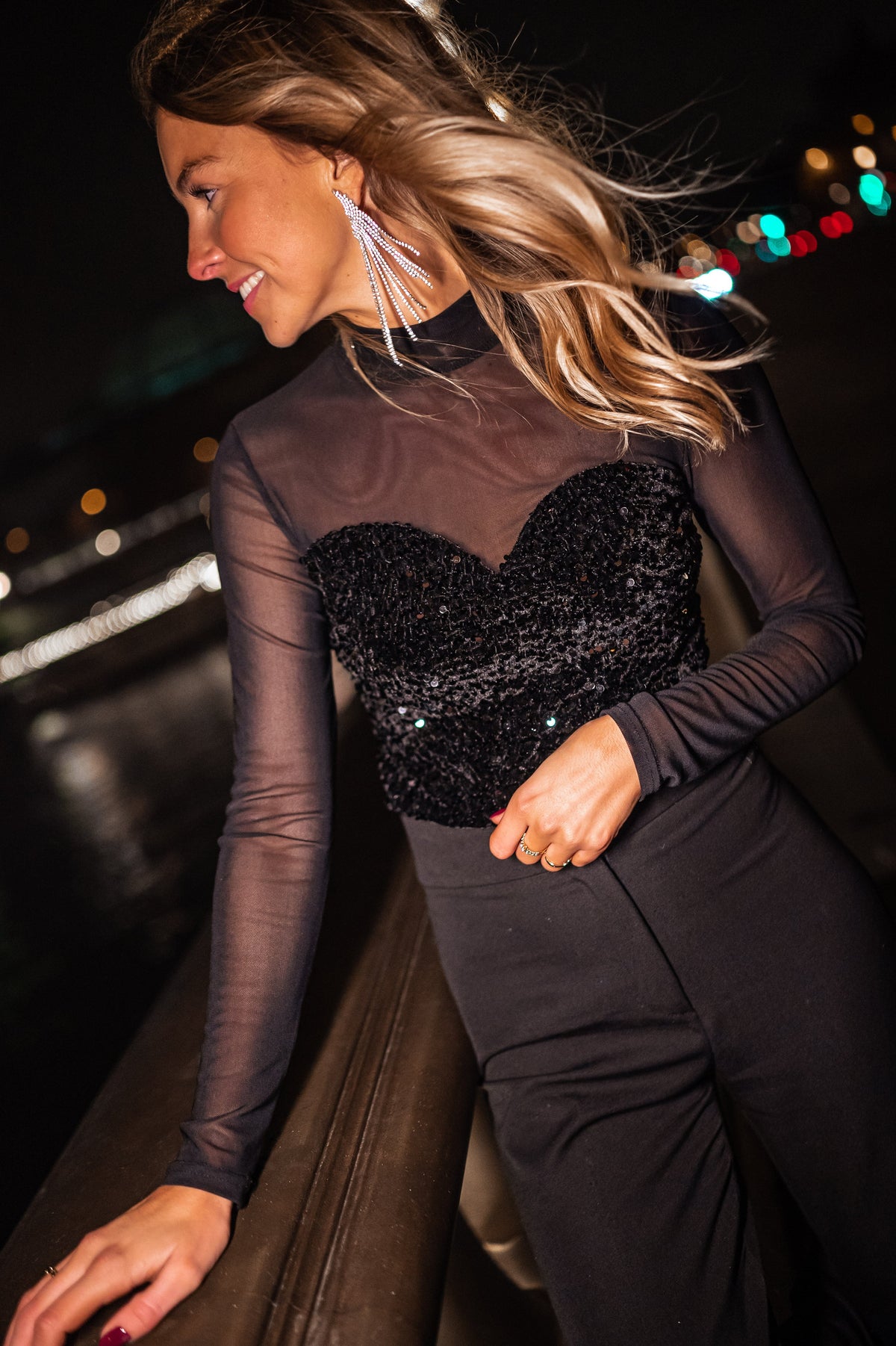 Blouse en velours à paillettes portée par une femme, vue rapprochée, col transparent, rambarde, de nuit