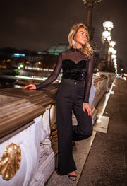 Blouse en velours à paillettes portée par une femme, silhouette entière, pont, pantalon noir, de nuit