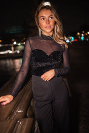 Blouse en velours à paillettes portée par une femme, vue de trois-quarts, main sur la rambarde, de nuit
