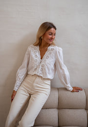 Blouse brodée aux poignets portée par une femme, assise, sur un canapé, pantalon beige