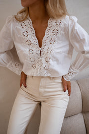 Blouse brodée aux poignets portée par une femme, vue rapprochée, broderie ajourée, pantalon beige