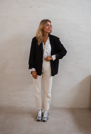 Blouse brodée aux poignets portée par une femme, silhouette entière, blazer noir, baskets, de loin
