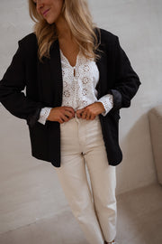 Blouse brodée aux poignets portée par une femme, vue rapprochée, blazer noir ouvert