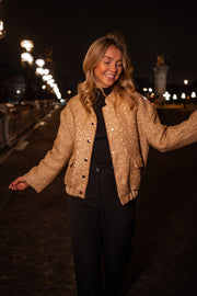 Bomber entièrement pailleté porté par une femme, vue de trois-quarts, de nuit, bras écartés, pantalon noir