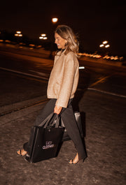Bomber entièrement pailleté porté par une femme, en marchant, de nuit, grand sac noir à la main