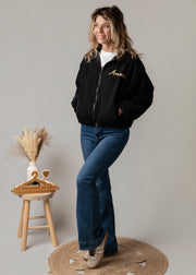 Bombers oversize en velours côtelé porté par une femme, silhouette entière, jean flare, tabouret
