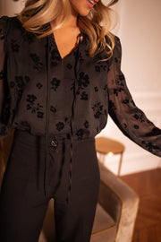 Blouse fleurie en velours portée par une femme, vue rapprochée, col noué, motifs fleurs