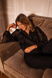 Blouse fleurie en velours portée par une femme, assise, fauteuil, sourire, main sur le visage