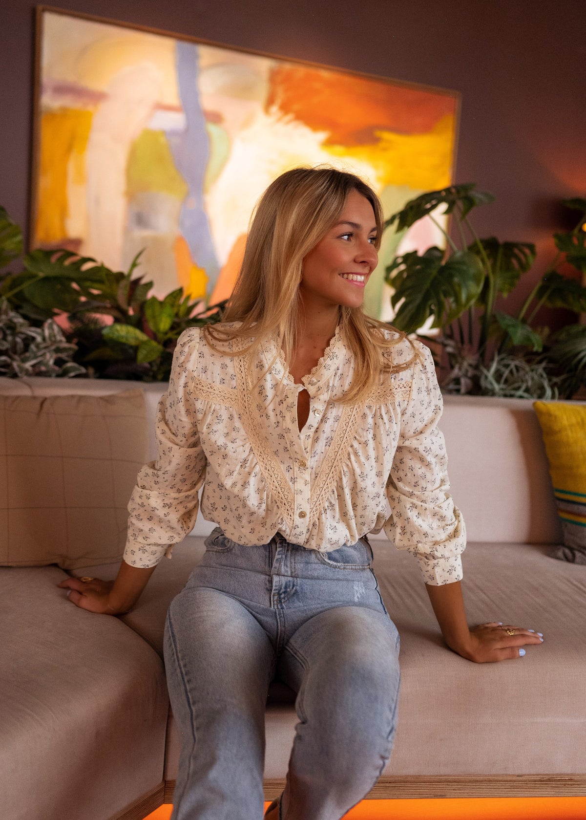 Chemise fluide à fleurs portée par une femme, assise, accoudée à un canapé, jean clair