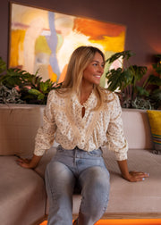 Chemise fluide à fleurs portée par une femme, assise, accoudée à un canapé, jean clair
