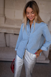 Chemise en jean à volant portée par une femme, vue de trois-quarts, pantalon argenté, sac bordeaux