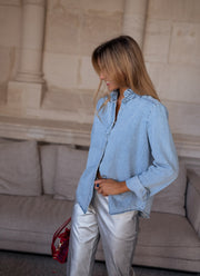 Chemise en jean à volant portée par une femme, vue de profil, pantalon argenté, sac bordeaux