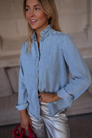 Chemise en jean à volant portée par une femme, vue de trois-quarts, mains dans les poches