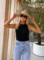 Top moulant col rond noir porté par une femme, silhouette entière, mains sur le chapeau
